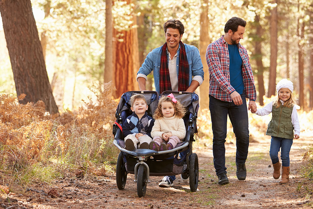 Same-sex male couple walking through the park with their kids