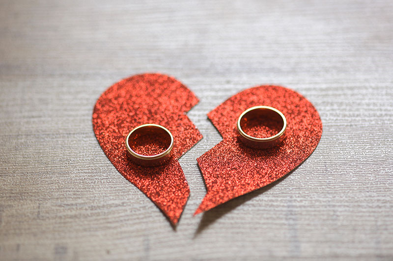 Broken red heart paper and wedding rings symbolizing divorce